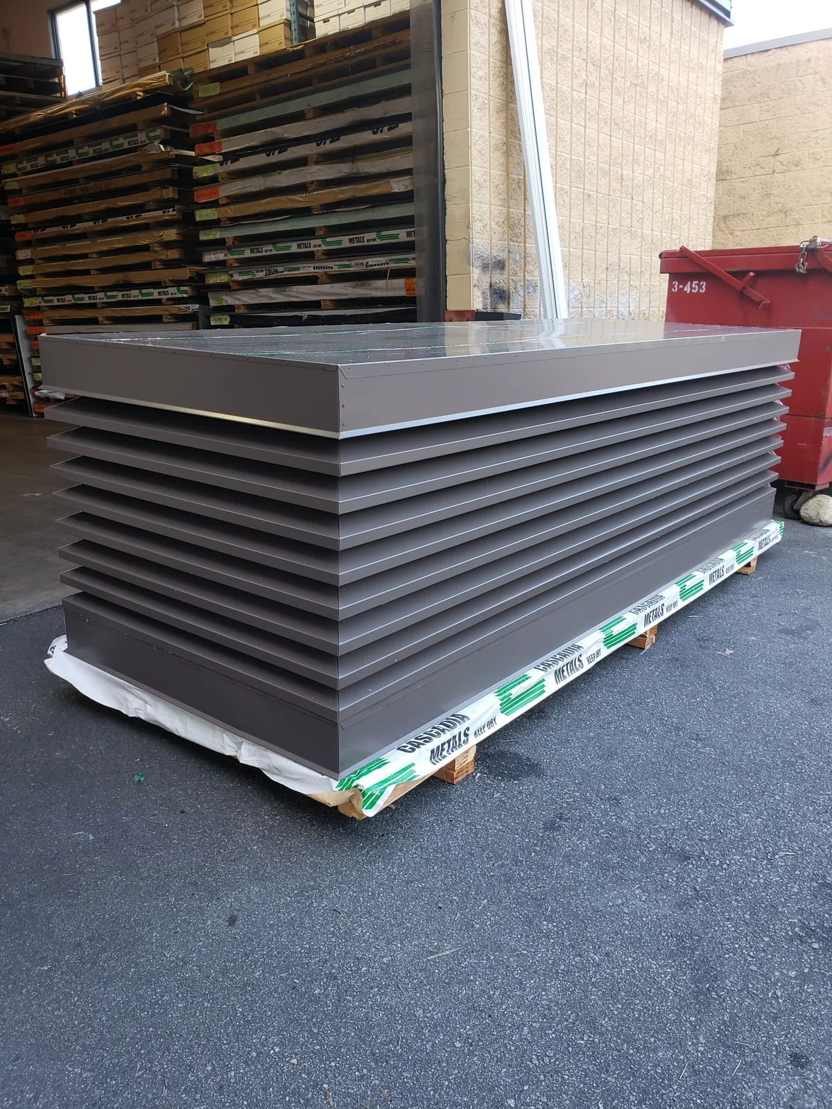 A tall stack of dark bronze louvered chimney caps on a pallet outside the shop, wrapped and ready to go out.